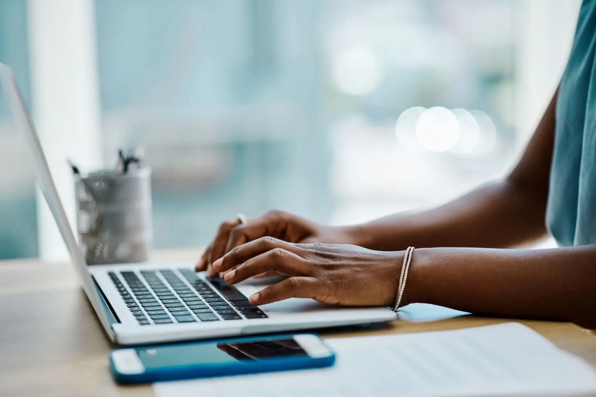 Person typing on a laptop at a desk with a smartphone and documents nearby.